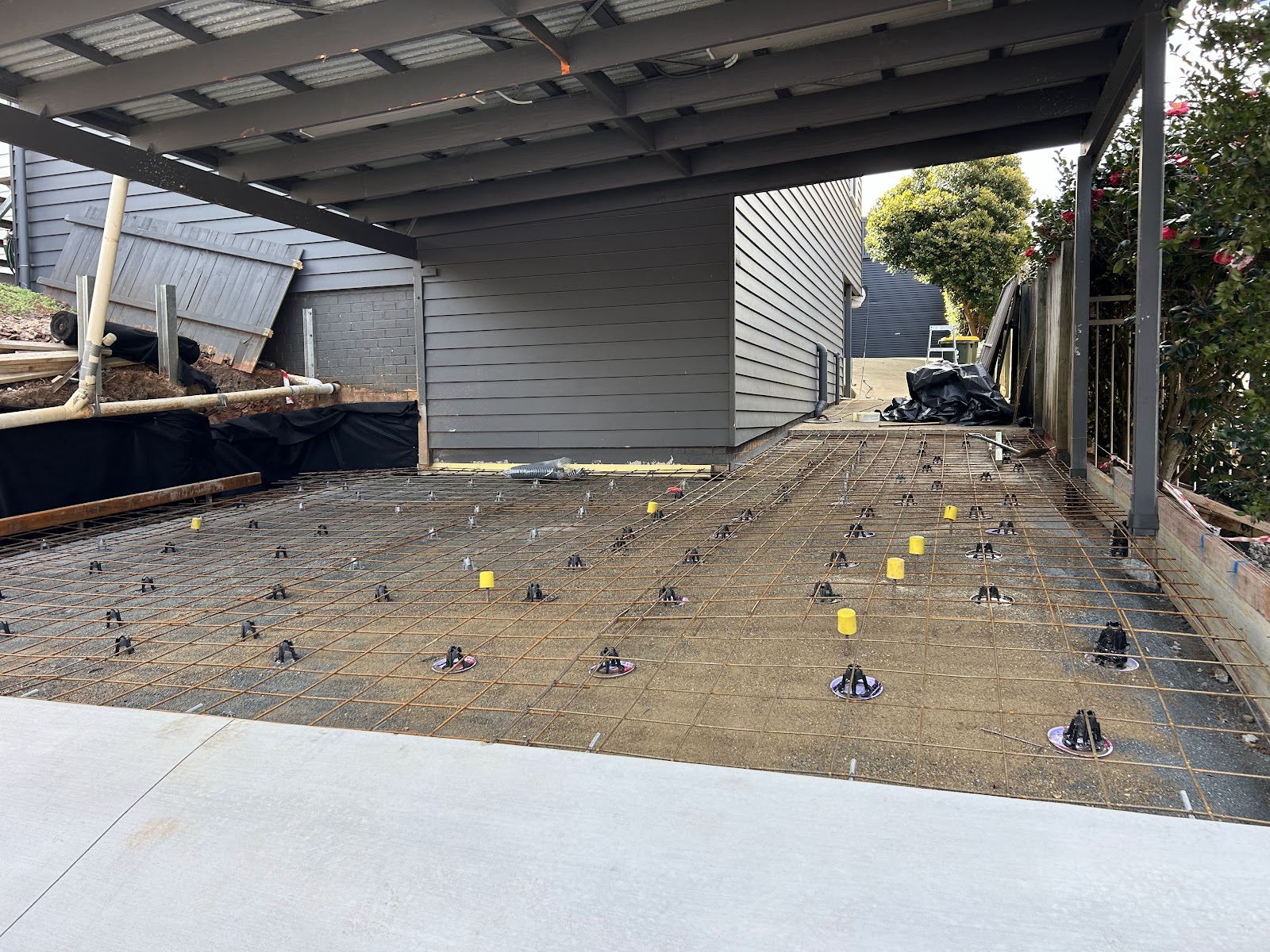 Steel mesh and bar chairs set out under a new carport beside a weatherboard house