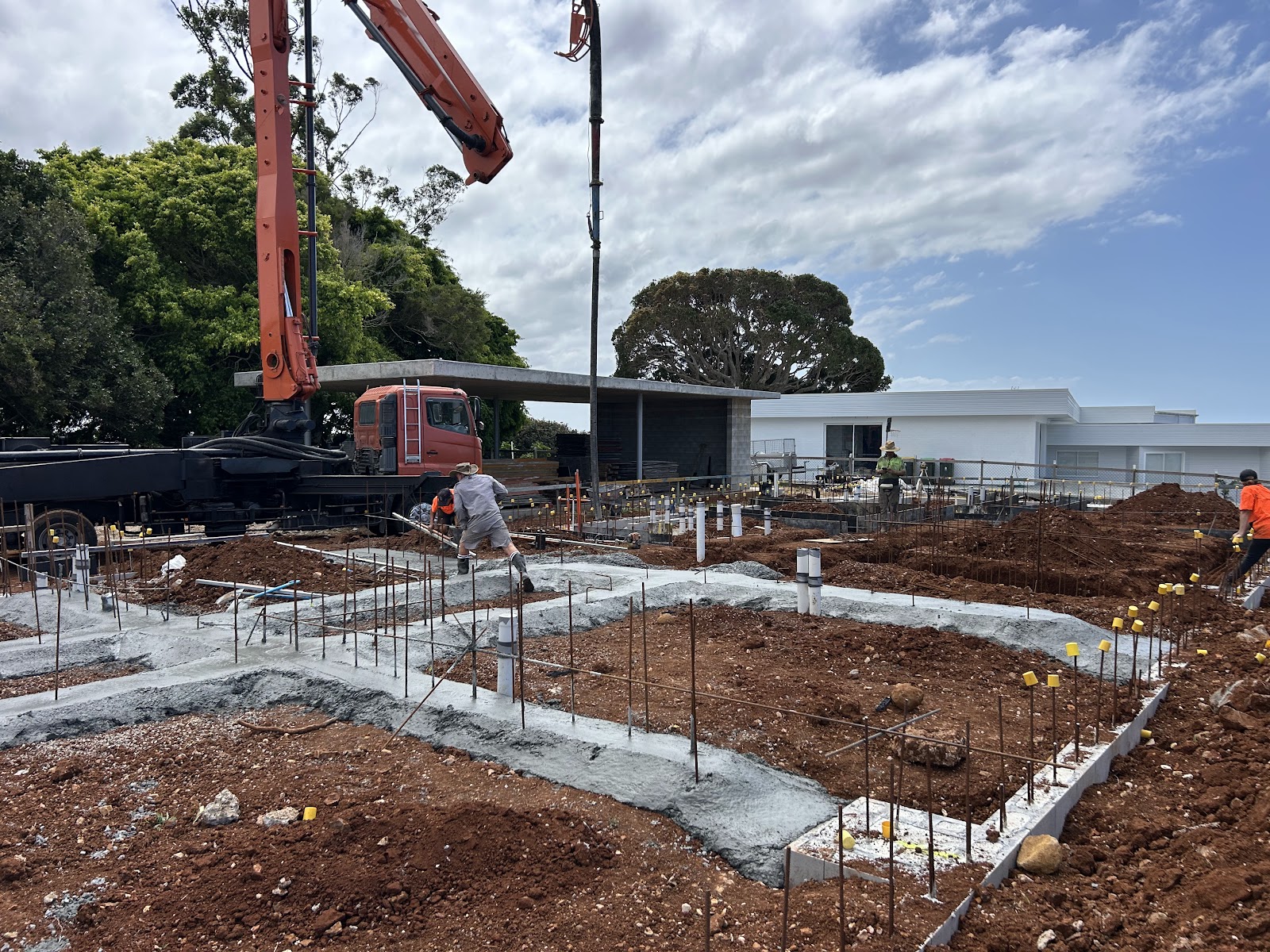 Strip footings being poured from a concrete pump boom on a red soil block