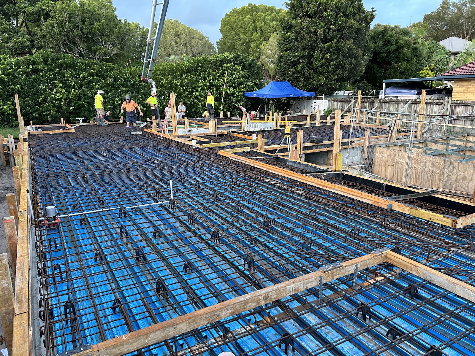 Large house slab set out with blue pods and steel mesh, crew and pump line on site